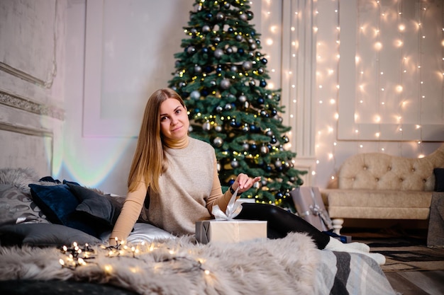 Eine junge Frau in einem Pullover mit langen schönen Haaren sitzt und lacht vor Weihnachtsgeschenken. Frohes Neues Jahr