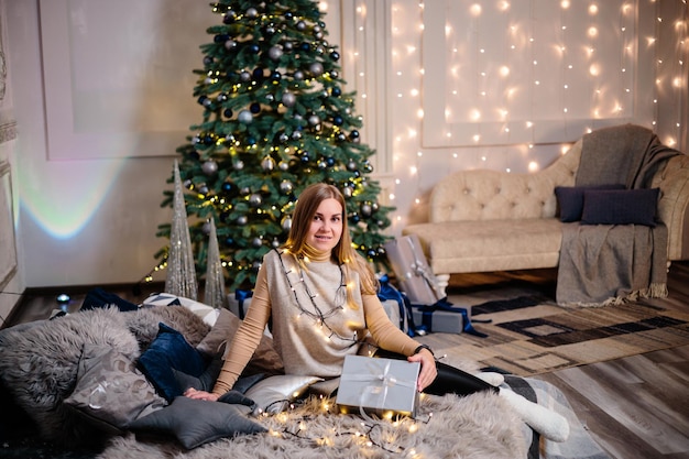 Eine junge Frau in einem Pullover mit langen schönen Haaren sitzt und lacht vor Weihnachtsgeschenken Frohes neues Jahr