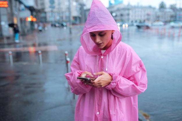 Eine junge Frau in einem Regenmantel schaut auf das Smartphone