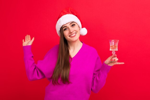 Eine junge Frau in einem rosa Pullover in einem Weihnachtsmann-Hut hält ein Glas Champagner Das Konzept, Weihnachten zu feiern