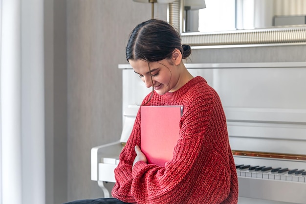 Eine junge Frau in einem roten Strickpullover neben einem weißen Klavier