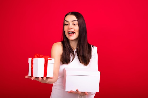 Eine junge Frau in einem schönen Abendkleid hält Geschenke für Weihnachten und Neujahr Brunette in einer guten Stimmung, die im Studio aufwirft