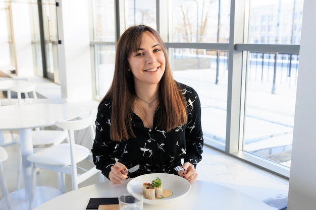 Eine junge Frau in einem schwarzen Kleid isst Brötchen in einem Café