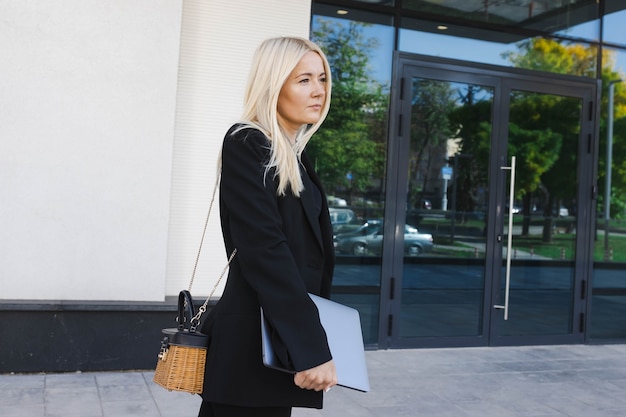 Eine junge Frau in einem stylischen Anzug mit einem Laptop geht in der Nähe eines Business Centers