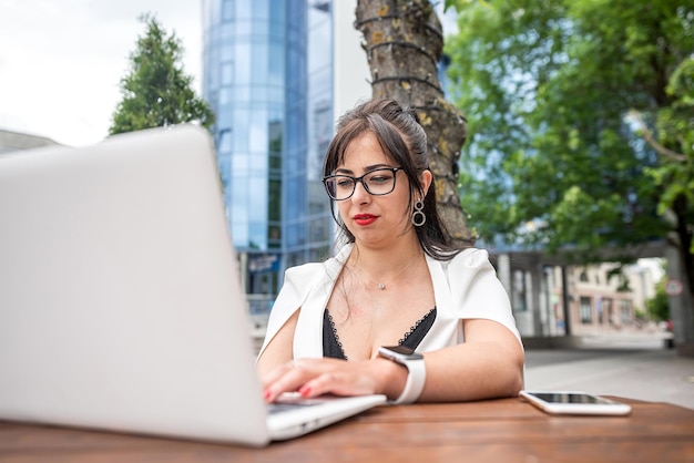 Eine junge Frau in einem weißen klassischen Anzug sitzt in einem Café und arbeitet mit einem Laptop