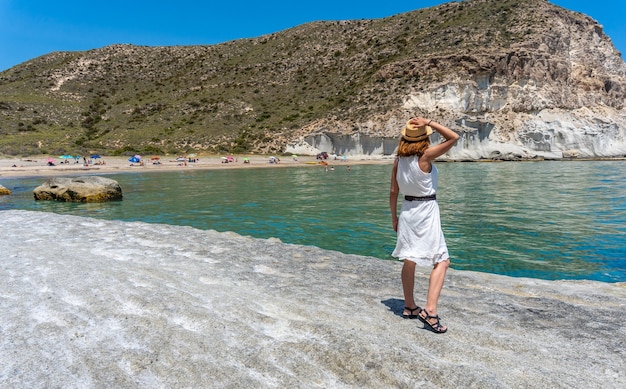 Eine junge Frau in einem weißen Kleid am Strand von Enmedio in Cabo de Gata an einem schönen Sommertag, Almería