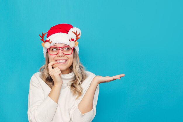 Eine junge Frau in einem weißen Pullover Weihnachtsmütze mit Weihnachtsbrille hält die Hand und schaut weg auf die leere Kopie
