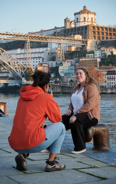 Eine junge Frau in einer farbenfrohen Jacke, die auf Reisen ein Foto von ihrer schönen Freundin macht