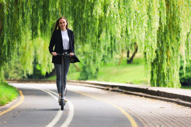 Eine junge Frau in stylischer Kleidung fährt mit einem Elektroroller auf einem Radweg