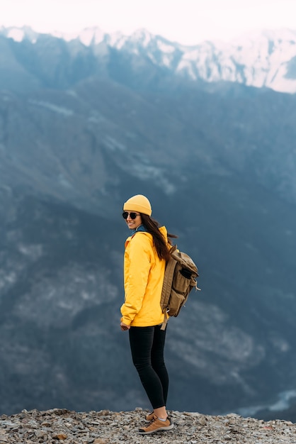 Eine junge Frau in Wanderausrüstung steht vor dem Hintergrund der Berge und schaut in die Kamera. Eine Frau zwischen den Bergen. Reisende Frau mit Rucksack auf dem Hintergrund der Berge. Platz kopieren