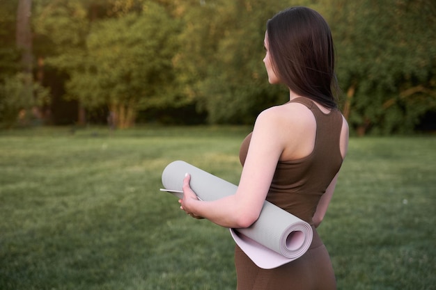 Eine junge Frau ist bereit, Yoga auf einer Matte im Park zu machen