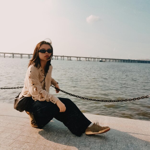 Eine junge Frau kämpft gegen Depressionen, trägt eine Sonnenbrille und sieht dem Himmel und der Meeresbrise gegenüber