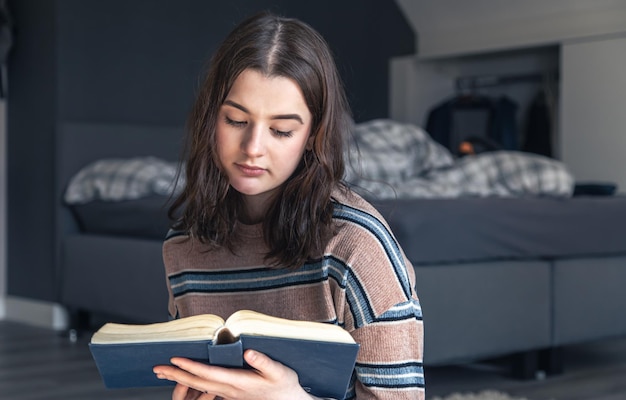 Eine junge Frau liest ein Buch, während sie in ihrem Zimmer auf dem Boden sitzt