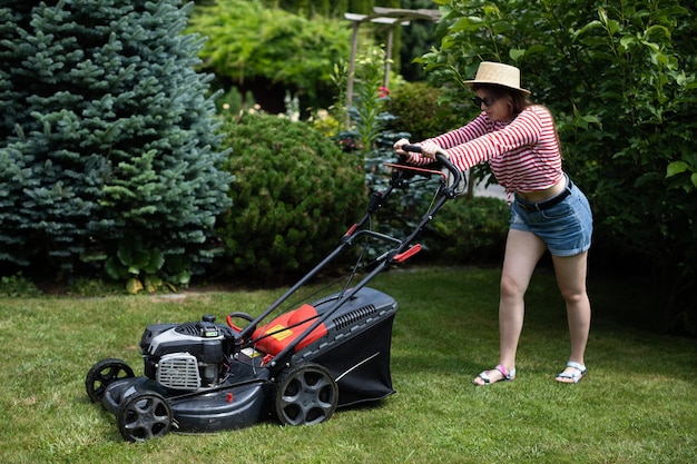 Eine junge Frau mäht an einem heißen Sommertag Gras mit einem Gartenmäher