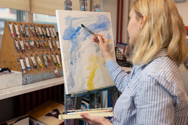 Eine junge Frau malt mit Aquarellfarben auf Leinwand