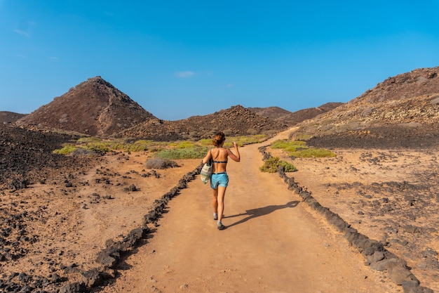 Eine junge Frau mit blauem Bikini auf dem Wanderweg nördlich der Isla de Lobos, nahe der Nordküste der Insel Fuerteventura, Kanarische Inseln. Spanien