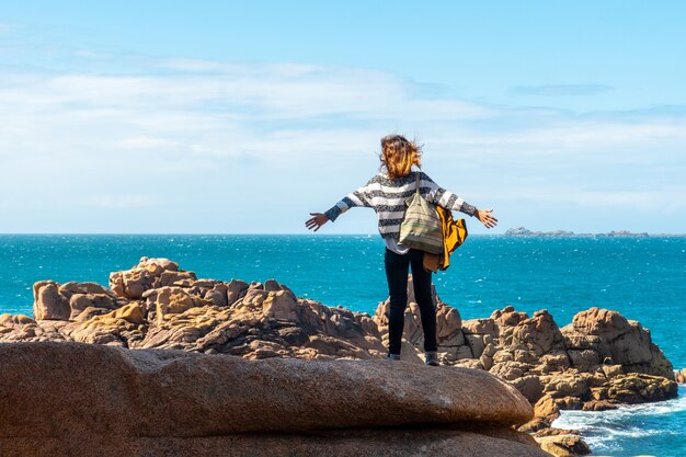 Eine junge Frau mit Blick auf das Meer entlang Lighthouse Mean Ruz, Hafen von Ploumanach, in der Stadt Perros-Guirec, Cotes-d'Armor, in der französischen Bretagne, Frankreich.