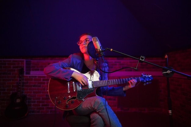 Eine junge Frau mit Brille, die Gitarre spielt und in Neonbeleuchtung singt