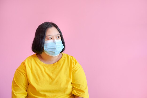 Eine junge Frau mit Down-Syndrom Tragen Sie eine Maske zum Schutz vor dem COVID-19-Coronavirus. Sie ist eine Studentin der Zerebralparese namens Down-Syndrom. Sie trug ein gelbes Kleid