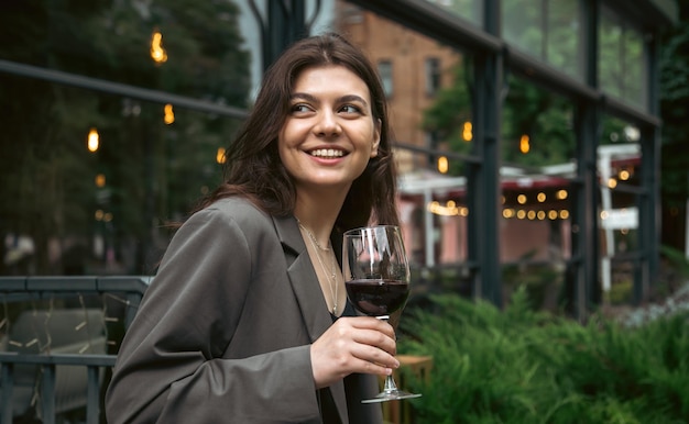 Eine junge Frau mit einem Glas Wein draußen in der Nähe eines Restaurants