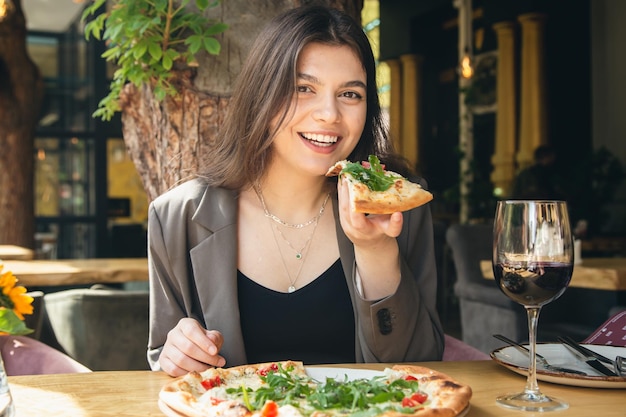 Eine junge Frau mit einem Glas Wein und einem Stück Pizza in einem Restaurant