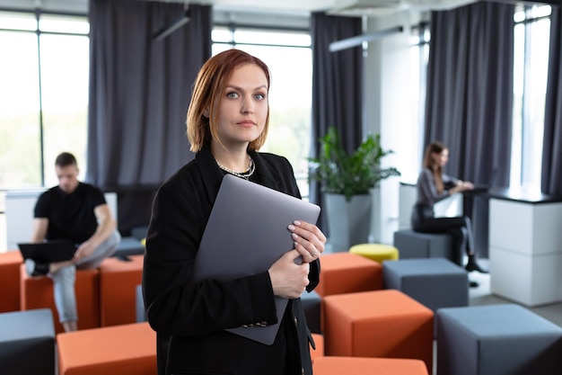 Eine junge Frau mit einem Laptop vor dem Hintergrund eines Arbeitsbüros