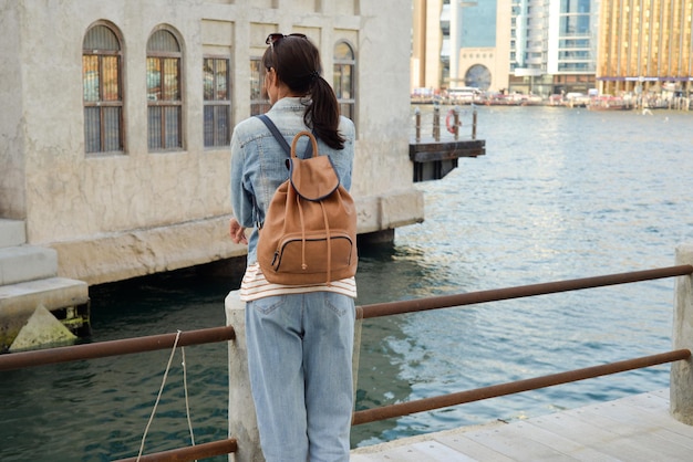 Eine junge Frau mit einem Rucksack auf dem Rücken bewundert den Fluss in der alten Dubai Creek Back View