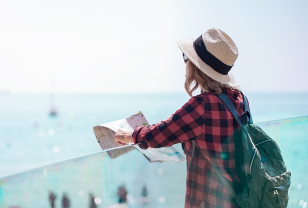 Eine junge Frau mit einem Rucksack, die auf der Fußgängerbrücke nahe Seehafen von Alicante bleibt und eine Karte liest