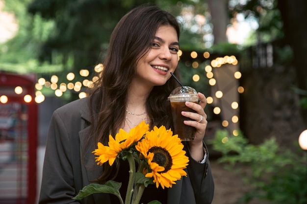 Eine junge Frau mit einem Strauß Sonnenblumen und einem kalten Kaffeegetränk in der Stadt