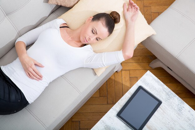 Eine junge Frau mit einem Tablet-PC auf dem Sofa.