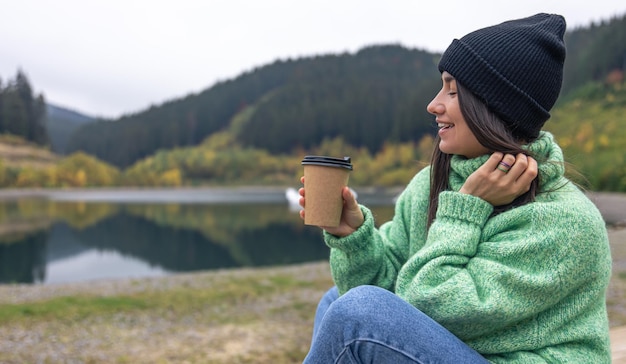 Eine junge Frau mit einer Tasse Kaffee auf einem verschwommenen Hintergrund von Bergen