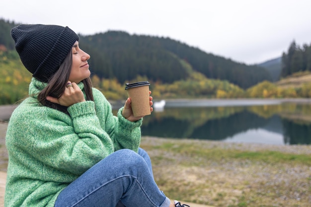 Eine junge Frau mit einer Tasse Kaffee auf einem verschwommenen Hintergrund von Bergen
