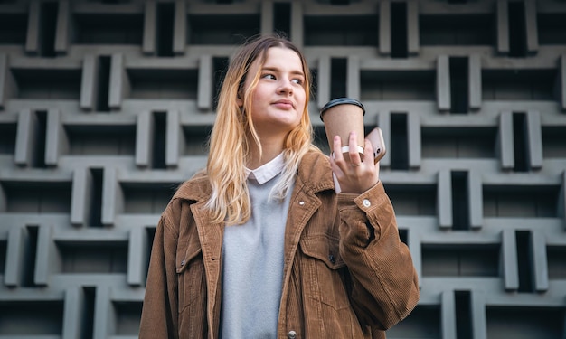 Eine junge Frau mit einer Tasse Kaffee und einem Smartphone im Hintergrund einer Wand