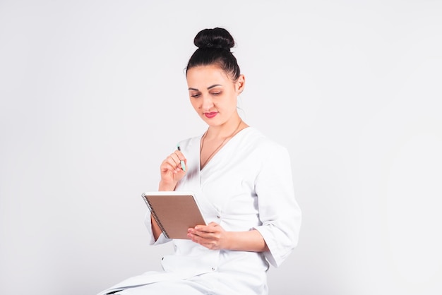 Eine junge Frau mit europäischem Aussehen in einer weißen medizinischen Uniform mit einem Notizbuch in der Hand Buchung einer Massagesitzung