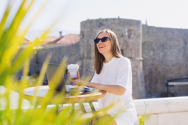 Eine junge Frau mit guter Laune arbeitet aus der Ferne in einem Café Sommercafé freiberuflich und im Tourismus