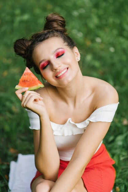 Eine junge Frau mit hellem Make-up schloss die Augen, lächelte und hielt eine Scheibe Wassermelone in den Händen