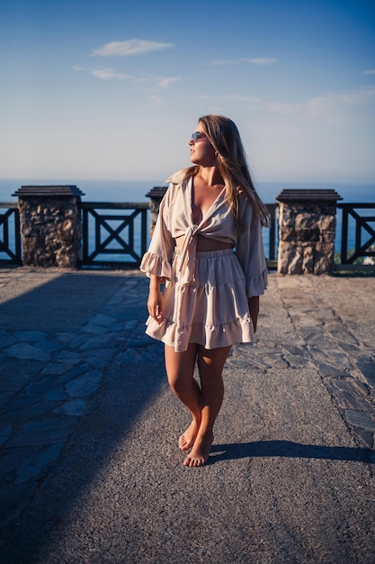 Eine junge Frau mit langen blonden Haaren in einem Oberteil und einem Rock geht an einem sonnigen Sommertag spazieren. Glückliches Mädchen mit einem Lächeln im Gesicht und in einer Sonnenbrille geht an einem sonnigen Tag spazieren