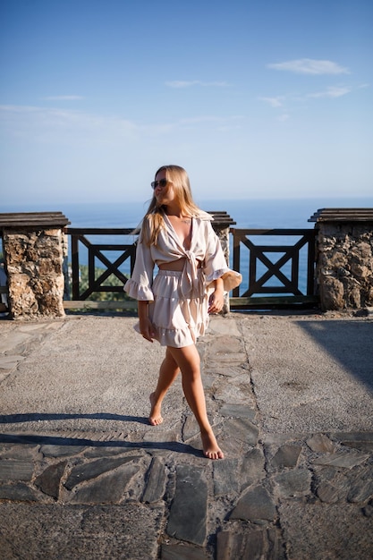 Eine junge Frau mit langen blonden Haaren in einem Top und einem Rock geht an einem sonnigen Sommertag spazieren. Fröhliches Mädchen mit einem Lächeln im Gesicht und Sonnenbrille geht an einem sonnigen Tag spazieren