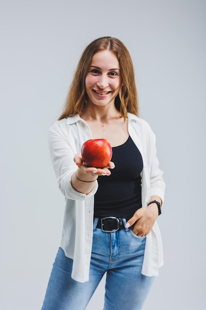 Eine junge Frau mit langen brünetten Haaren, gekleidet in ein weißes Hemd und Jeans, hält einen frischen roten Apfel in ihren Händen Gesundes Lebensmittelkonzept Weißer Hintergrund