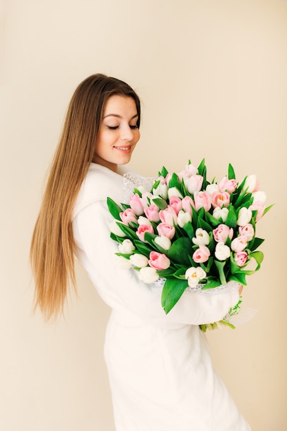 Eine junge Frau mit langen Haaren in einem weißen Schlafrock mit einem schönen und zarten großen Strauß rosa Tulpen.