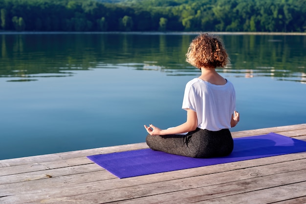 Eine junge Frau mit lockigem Haar, die draußen Yoga macht