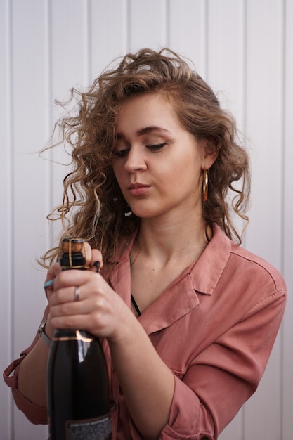 Eine junge frau mit lockigem haar öffnet eine flasche champagner. sie ist drinnen auf weißem hintergrund