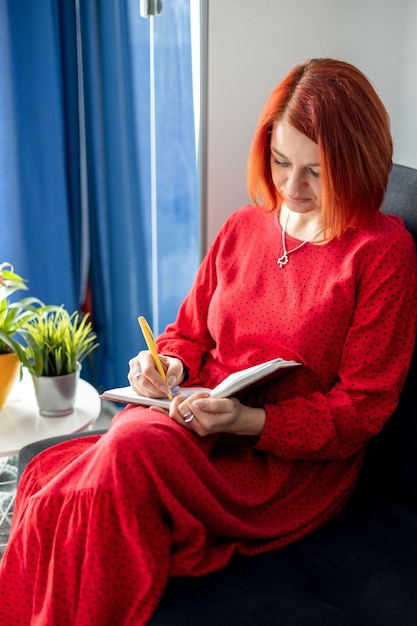 eine junge Frau mit roten Haaren sitzt auf einer Couch und macht Notizen in einem Notizbuch