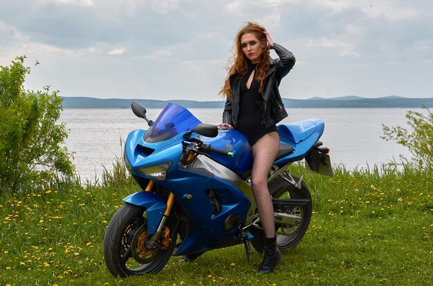 Eine junge Frau mit roten Haaren und schwarzer Lederjacke auf einem blauen Sportmotorrad