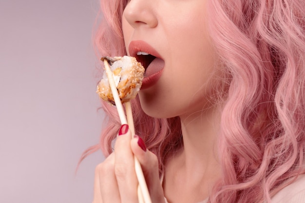 Eine junge Frau mit roten Nägeln und rosa Haaren isst Sushi
