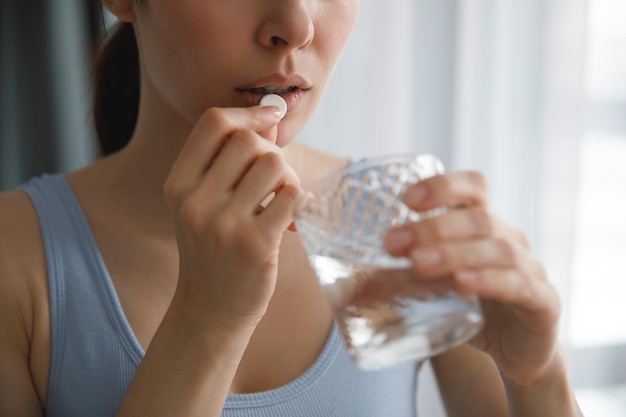 Eine junge Frau nimmt Medikamente oder Vitamine ein. Sie hält ein Glas Wasser