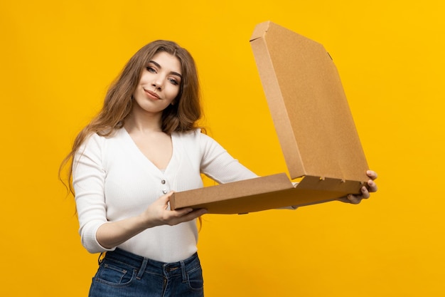 Eine junge Frau öffnet eine Pizzaschachtel auf gelbem Hintergrund Die Freude an leckerem Essen Schnelle Lieferung