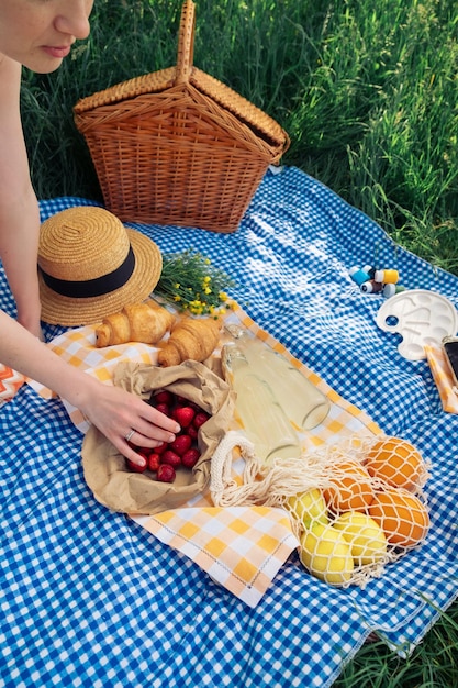 Foto eine junge frau pflückt bei einem picknick in der natur eine erdbeere, während sie auf einer blauen decke sitzt