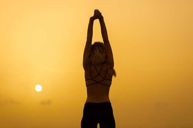 Eine junge Frau praktiziert bei Sonnenaufgang Yoga an der Meeresküste