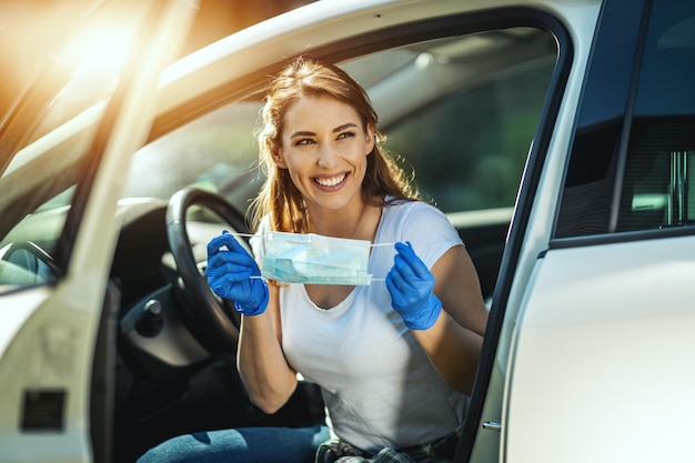 Eine junge Frau setzt eine Maske auf ihr Gesicht, um eine Infektion während des Ausbruchs des Grippevirus und der Coronavirus-Epidemie zu vermeiden, und macht sich bereit, mit dem Auto zur Arbeit zu fahren.